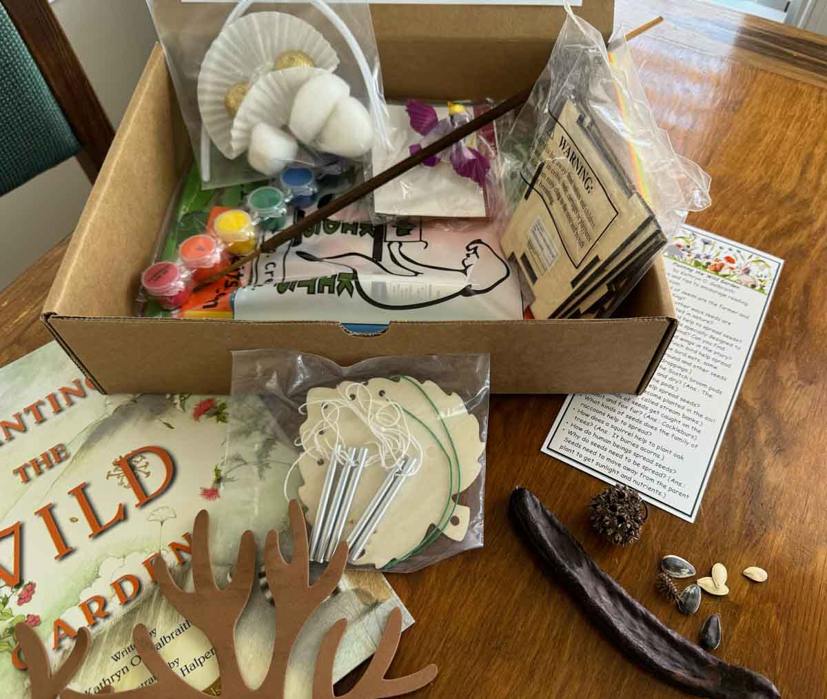 An open cardboard box with supplies for crafts to go along with the book Planting the Wild Garden which is with the supplies.