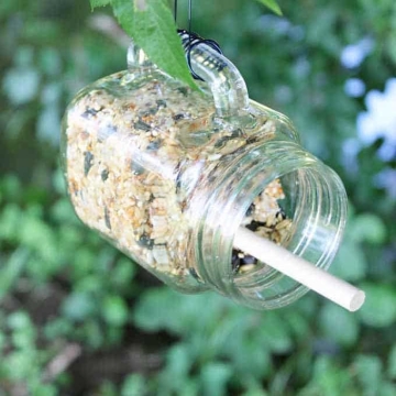 Bird seed and a dowel in a horizontal hanging mason jar glass.